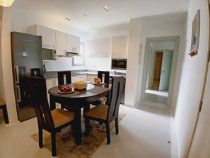 A modern kitchen with white cabinets, a round dining table with four chairs, and a refrigerator. - El Gouna Swan Lake on the shores of the Crystal Lagoon, conference room, 10 minutes from downtown, marina (Hurghada Al-Bahr al-ahmar)