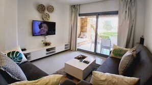Un salon moderne doté d’un téléviseur à écran plat fixé au mur, d’un canapé, d’une table basse et d’une porte-fenêtre coulissante donnant sur un espace extérieur.