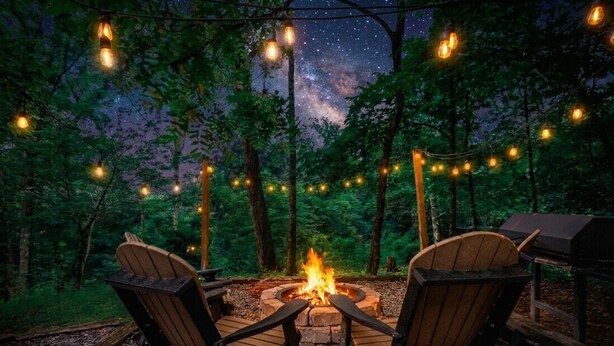 A campfire with chairs around it, surrounded by trees and string lights. - Pet Friendly · Hot Tub · Mins to Dollywood · Views (Pigeon Forge)