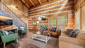 A log cabin interior with a staircase, green and beige sofas, a coffee table, and wooden walls. - Pet Friendly · Hot Tub · Mins to Dollywood · Views (Pigeon Forge)