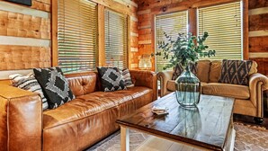 A cozy log cabin interior with a brown leather sofa, a wooden coffee table, and a vase with greenery. - Pet Friendly · Hot Tub · Mins to Dollywood · Views (Pigeon Forge)