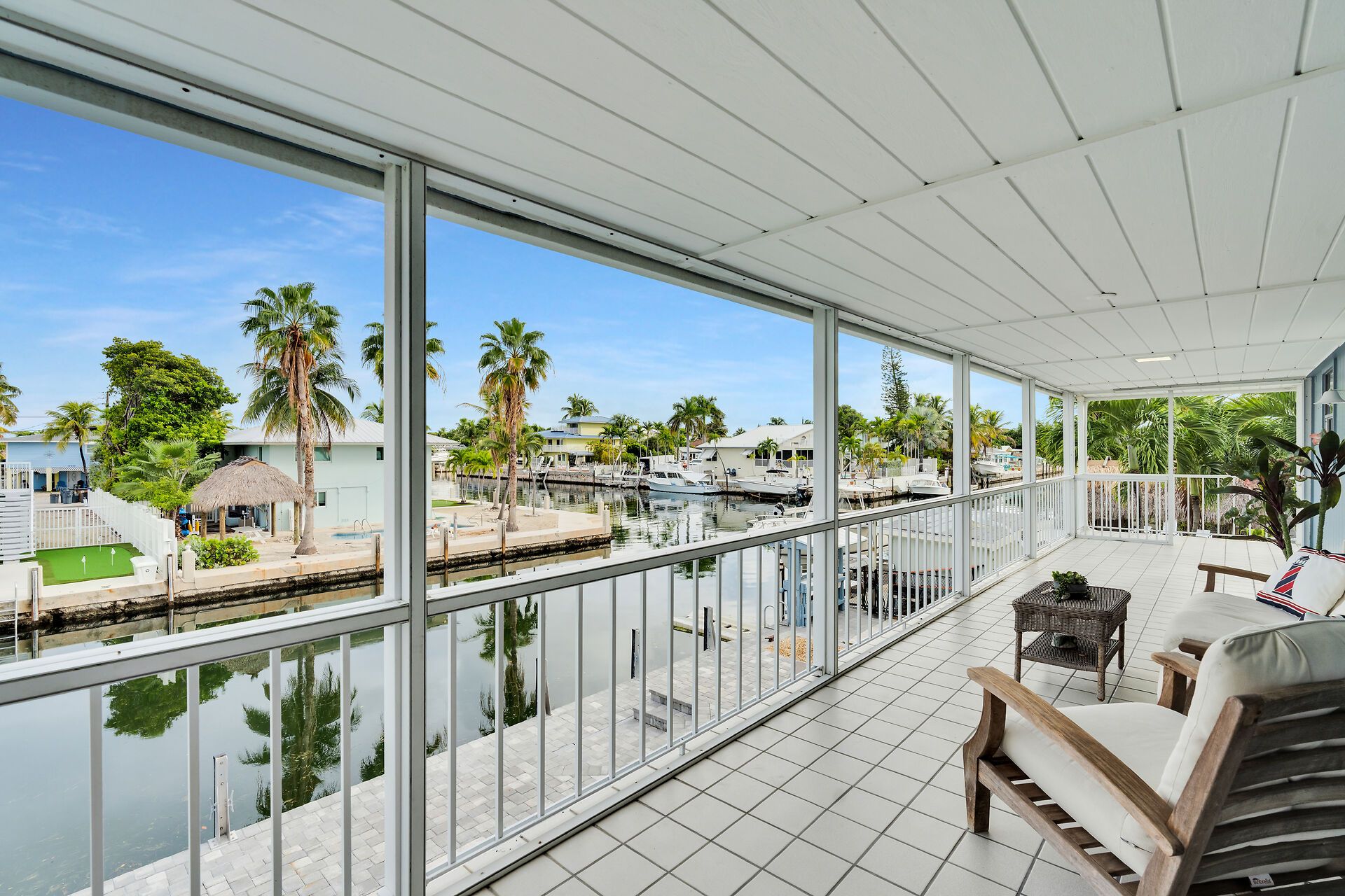 A covered balcony with a view of a marina, palm trees, and a pool.