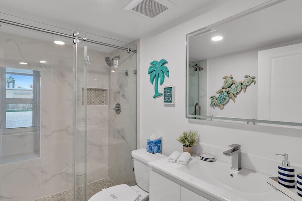 A modern bathroom with a glass-enclosed shower, a large mirror, and a vanity with a sink and towel rack.