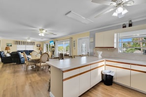 A spacious living area with a dining table, sofas, and a kitchen with white cabinets and a wooden countertop.