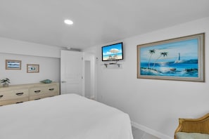 A bedroom with a bed, a television mounted on the wall, and a painting of a beach scene.