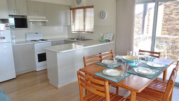 A compact kitchen with white appliances, a dining table set for four, and a view of the outside.