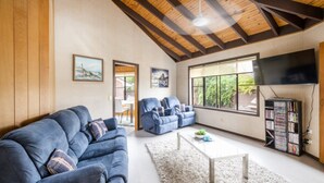A living room with a high ceiling, a fireplace, a television, and a bookshelf. - The Peninsula - Lifestyle Yamba (YAMBA)