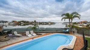 A swimming pool with lounge chairs and a view of a lake with boats. - The Peninsula - Lifestyle Yamba (YAMBA)
