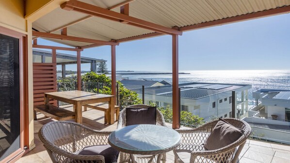 Ein Balkon mit Tisch und Stühlen, der Blick auf die Küste freigibt.