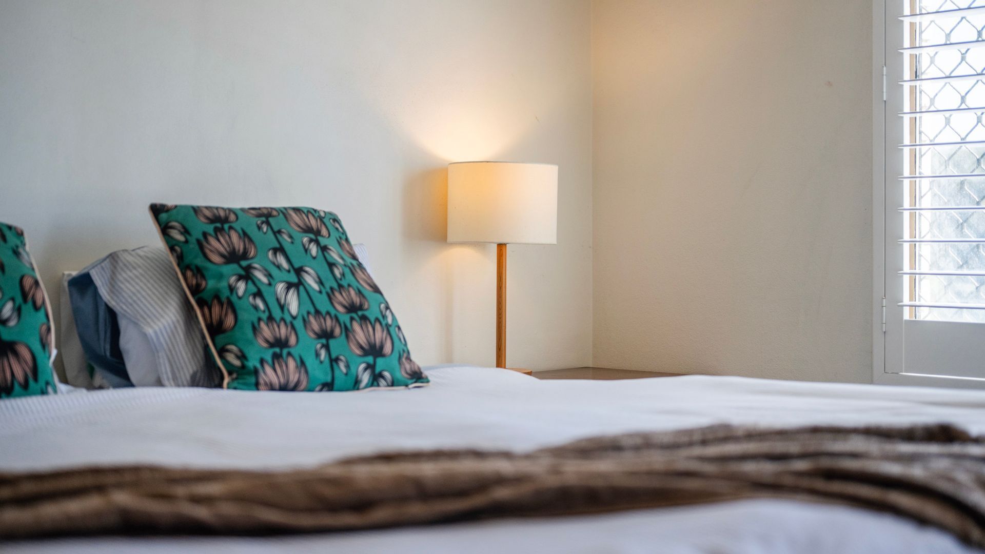 Una cama bien tendida con un cojín estampado y una lámpara de noche.