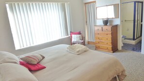 A bedroom with a bed, a chair, a dresser, and a bathroom visible through an open door. - Flinders Lodge Unit 3 - Lifestyle Yamba (YAMBA)