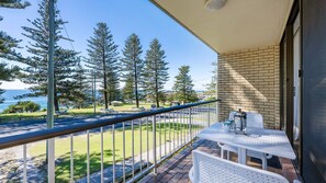 Un balcone con tavolo e sedie, affacciato su un parco alberato e con vista sul mare.