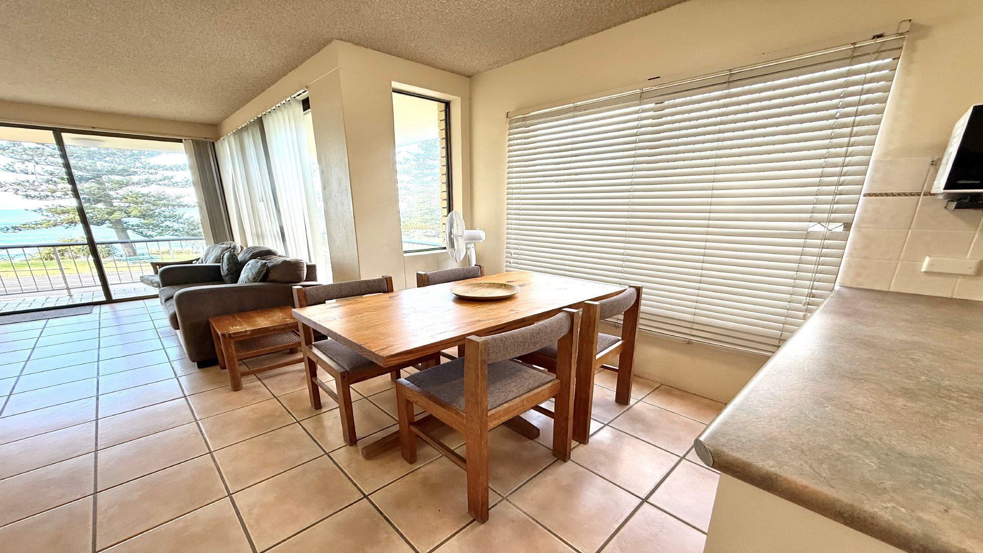 Un comedor con una mesa y sillas de madera, un sofá, y vistas a través de amplios ventanales.