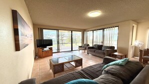 Un salon spacieux avec un grand canapé, un téléviseur posé sur un meuble en bois et une table basse en verre.