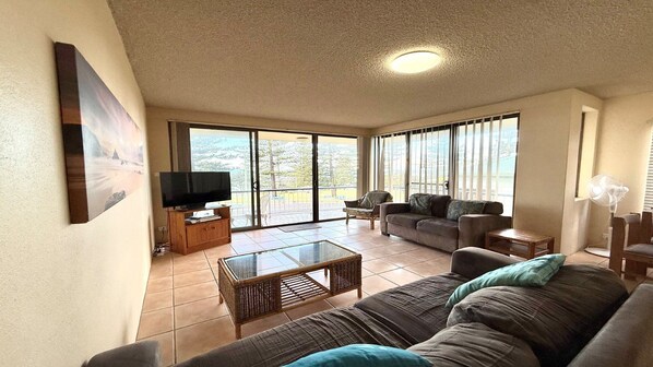 A spacious living room with a large sofa, a television on a wooden stand, and a glass coffee table.