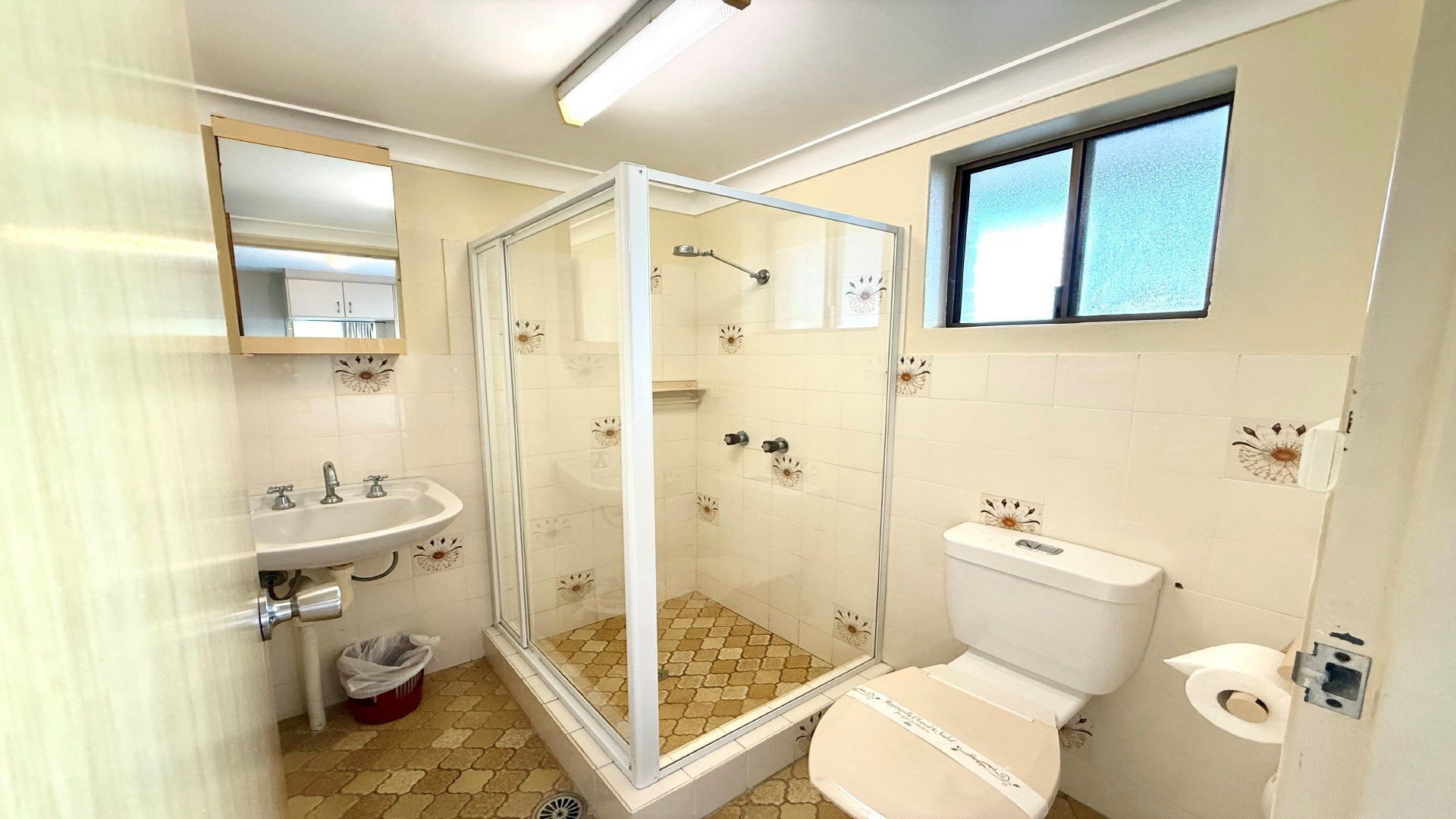 A bathroom with a glass-enclosed shower, a toilet, and a sink.