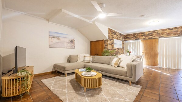 A living room with a sofa, a coffee table, a TV, and a ceiling fan.
