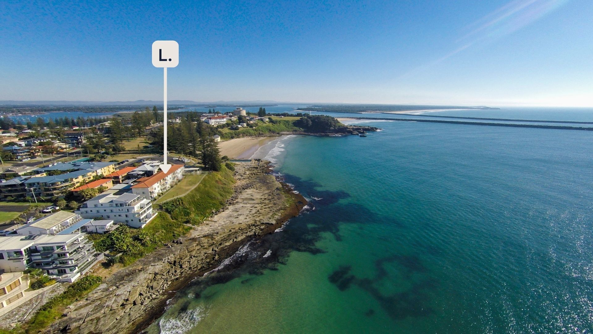 A coastal residential area with houses along the shoreline, a lighthouse, and a clear view of the sea.