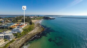 Una zona residenziale costiera con case lungo la battigia, un faro e una vista limpida sul mare.