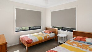 A bedroom with two single beds, a bedside table with a lamp, and a window with a view.