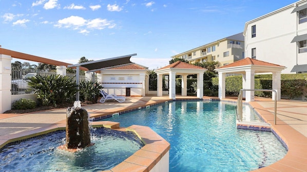 A swimming pool with a water fountain, lounge chairs, and a covered pavilion.