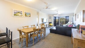 A dining area with a wooden table and chairs, a sofa, and a television.