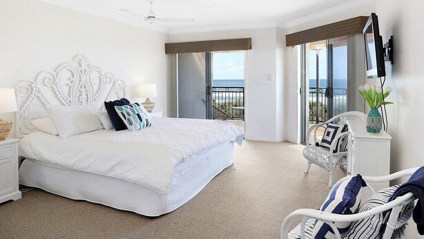 A hotel room with a large bed, a balcony with a view, and a seating area with a chair and a table. - Breakers Block 2 Unit 11 - Lifestyle Yamba (YAMBA)