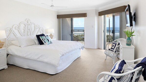 A hotel room with a large bed, a balcony with a view, and a seating area with a chair and a table.