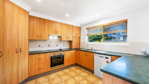 Una cocina con armarios de madera, estufa, lavavajillas y ventana con persianas.