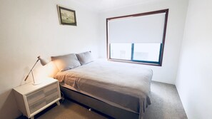 Quarto com cama, mesa de cabeceira, abajur e janela.