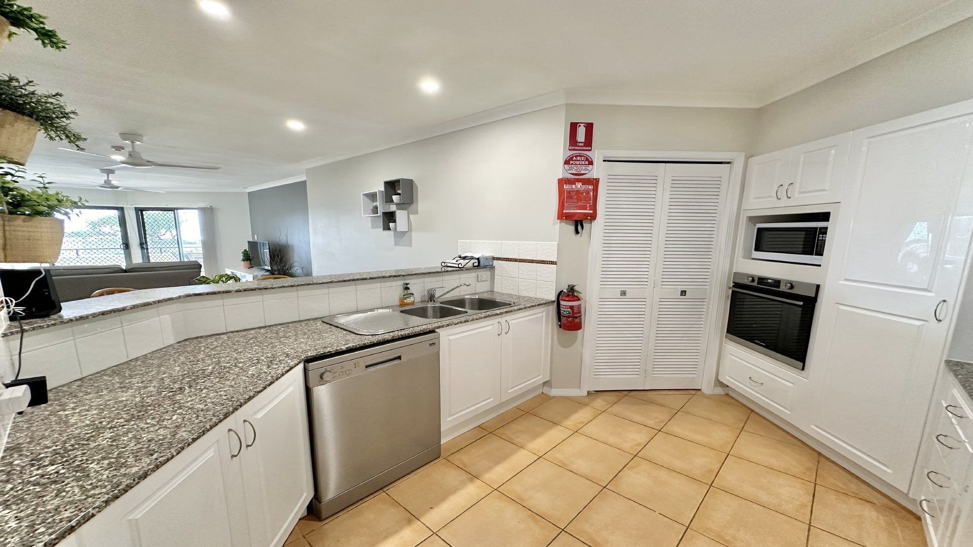 A modern kitchen with white cabinets, granite countertops, a dishwasher, a sink, and a fire extinguisher mounted on the wall.