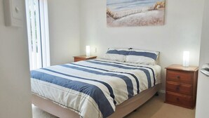 A bedroom with a bed, two bedside tables, a nightstand, a wall-mounted lamp, and a painting.