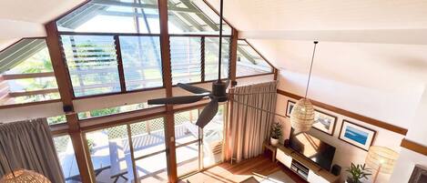 Amplia sala de estar con techos altos, ventanas grandes, ventilador de techo y televisor.