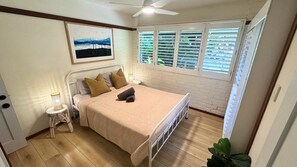 A bedroom with a bed, a nightstand, a ceiling fan, a window with blinds, and a painting on the wall.