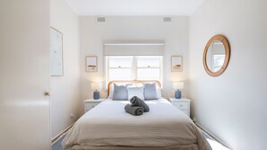 A bedroom with a bed, two bedside tables, a window, and a mirror on the wall.