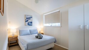 A bedroom with a bed, two bedside tables, a window, and a wardrobe.