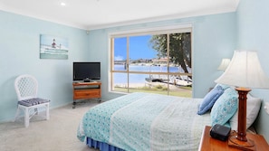 Enjoy a scenic view of the water from this hotel room, featuring a comfortable bed, a wicker chair, and a flat-screen TV.