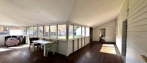 A room with a wooden floor, a table, chairs, and a windowed area.