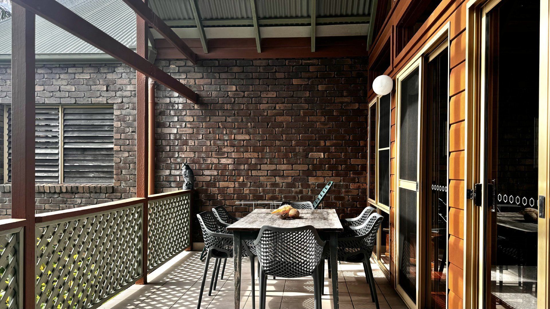 A covered outdoor seating area with a brick wall backdrop, a table with chairs, and a decorative bird statue.