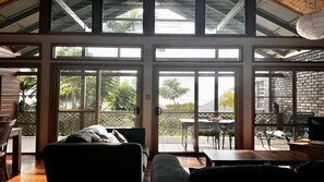 Une pièce spacieuse dotée de grandes portes-fenêtres coulissantes qui donnent sur un espace extérieur aménagé avec une table et des chaises en bois.