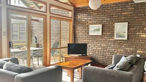 A living room with a brick wall, a television on a wooden table, and a sofa. - Drift - Lifestyle Yamba (ANGOURIE)