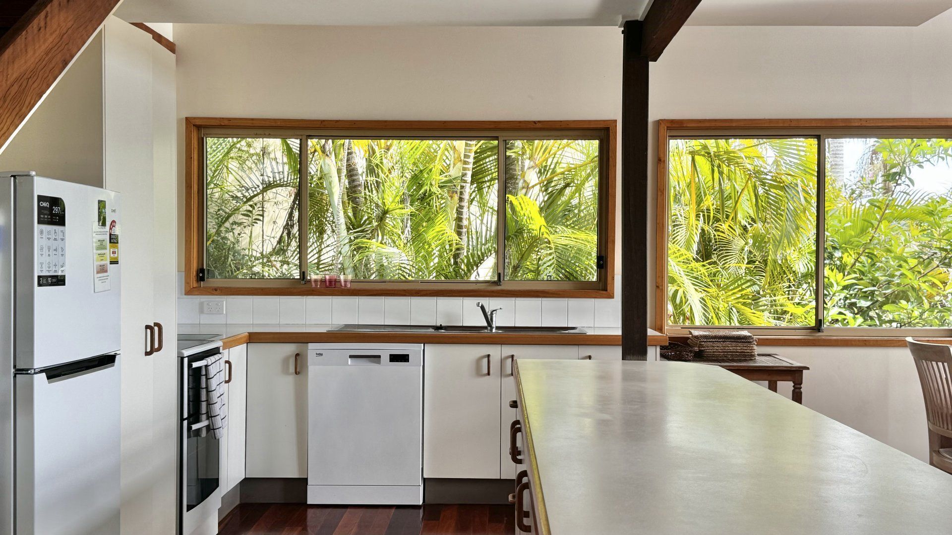 A modern kitchen with a built-in dishwasher, a refrigerator, and a window with a view of lush greenery.