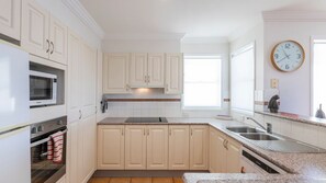 A modern kitchen with white cabinetry, a built-in oven, a microwave, a sink, and a clock on the wall. - Meridian 5 - Lifestyle Yamba (YAMBA)