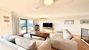 A living room with a sofa set, a coffee table, a flat-screen TV, and a sliding glass door leading to a balcony.