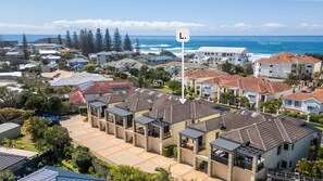 A residential area with multiple houses, a clear view of the ocean, and a sign indicating the location as Pippi Beach. - Meridian 5 - Lifestyle Yamba (YAMBA)