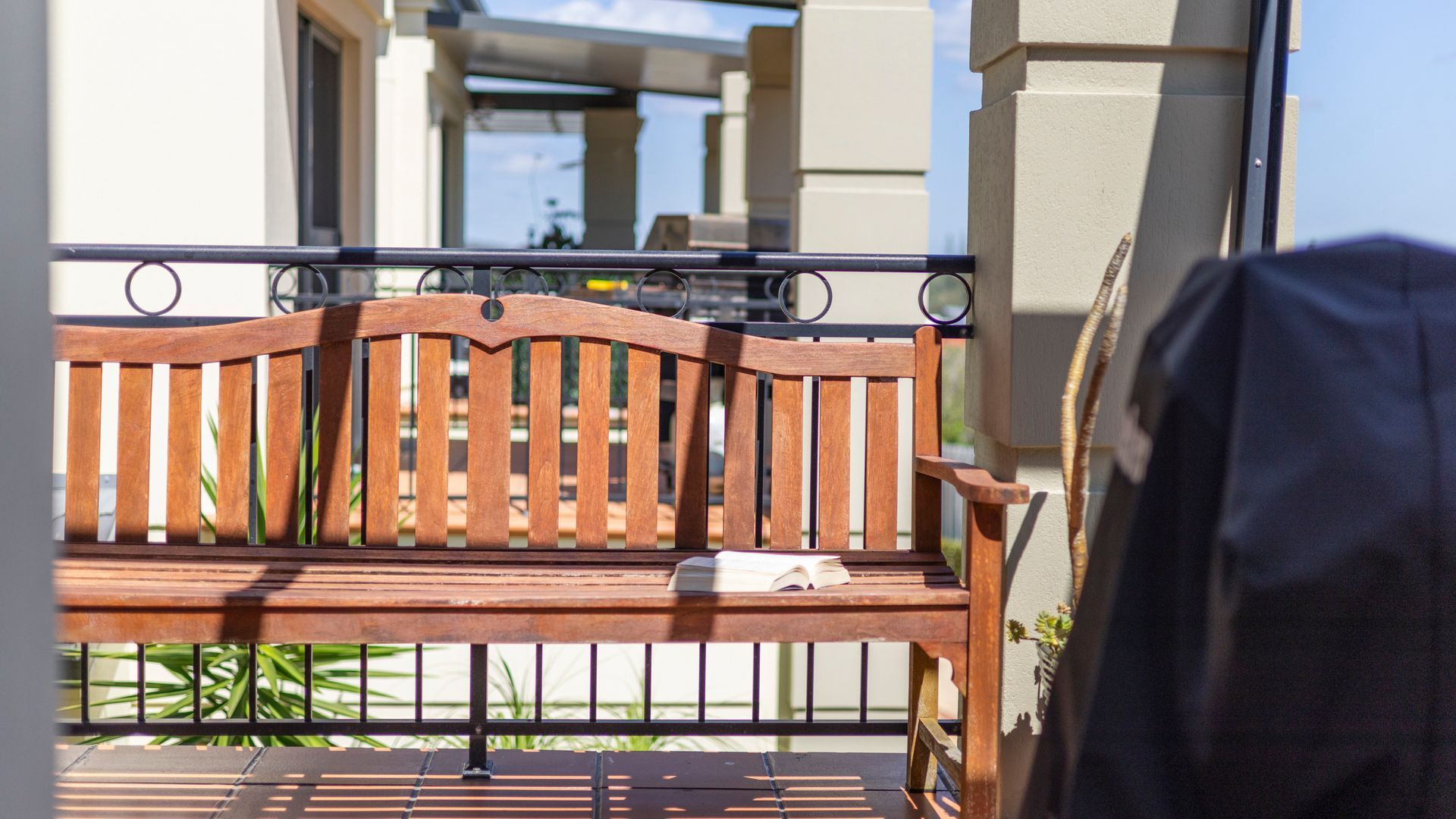Un banc en bois, sur lequel repose un livre, est placé sur un balcon doté d’une rambarde en métal.