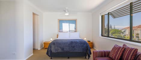 Un dormitorio con cama, mesita de noche, ventana con vistas y ventilador de techo.