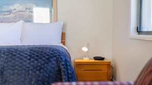 A bedroom with a bed, a nightstand with a lamp, and a window with a view of palm trees.