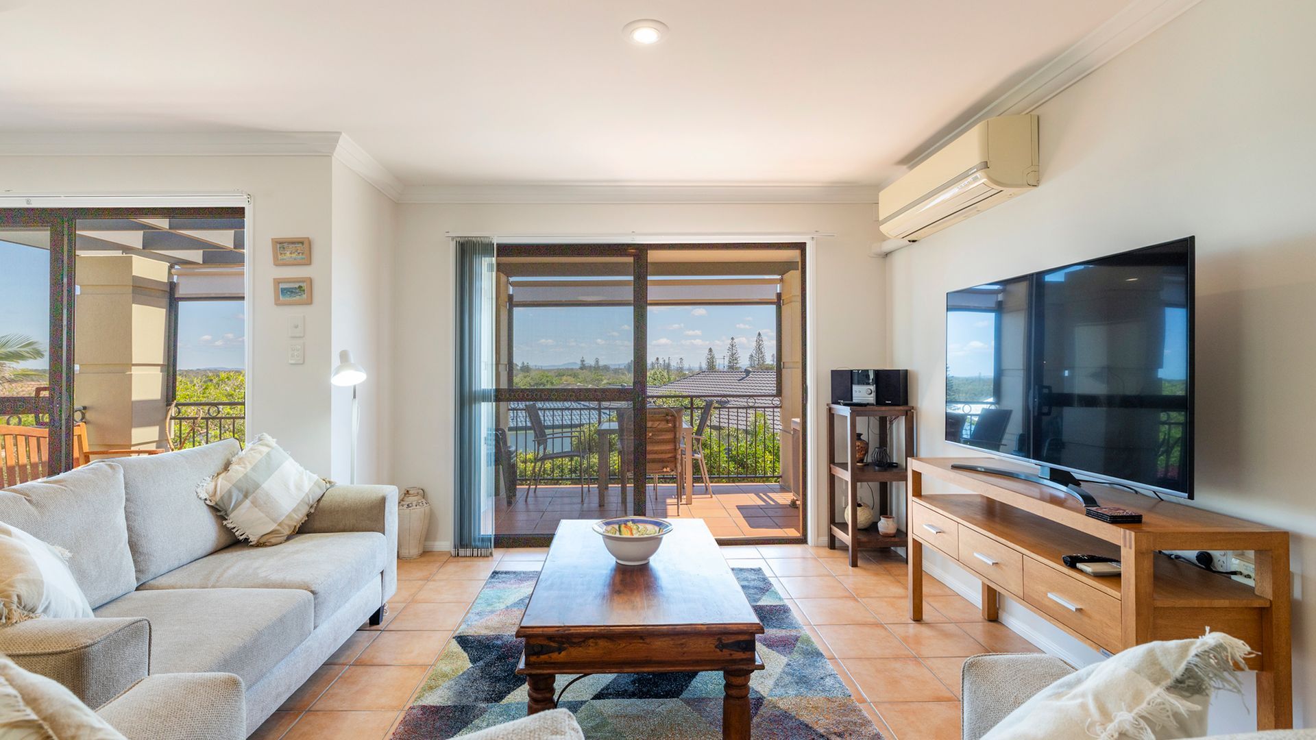 A living room with a sofa, a coffee table, a TV, and a balcony with a view.