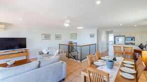 A modern living room with a flat-screen TV, a sofa, and a dining area with a table set for four.